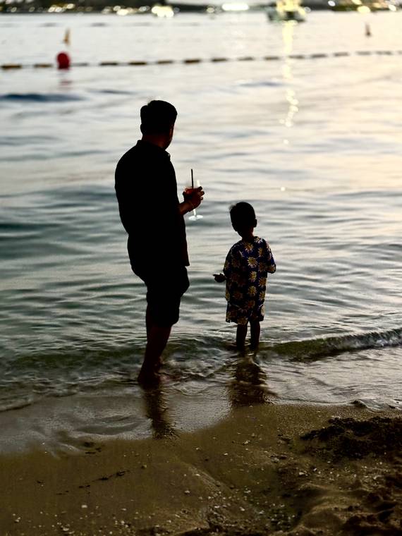 Silhouette of an adult and child at the water's edge in Dubai, UAE