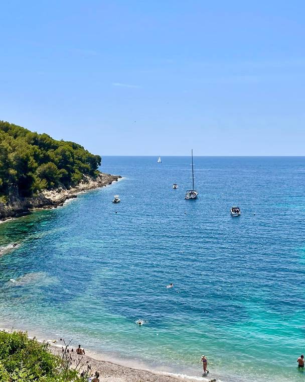 Sailboats in a turquoise cove below rocky cliffs in Monaco
