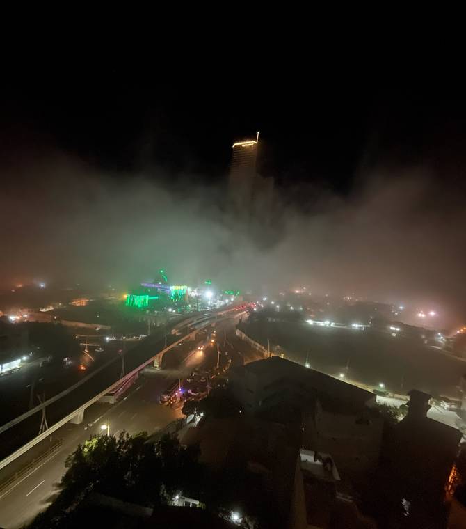 Night view of a lit hilltop monument in the fog above Karachi, Pakistan