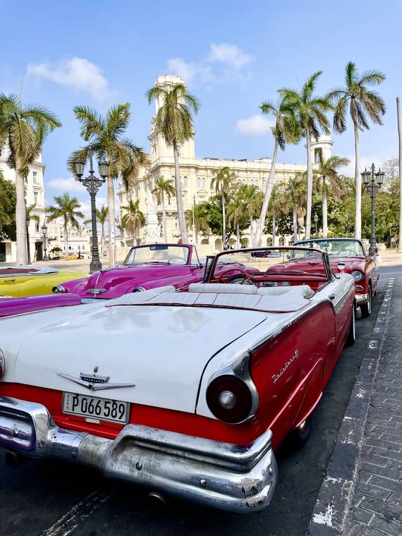 A vintage red convertible parked on a palm-lined street in Havana, Cuba